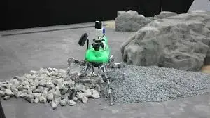 Robotic lunar excavator with green accents collecting moon rocks on gray lunar surface
