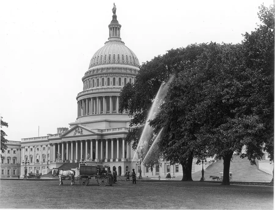 The United States Capitol building with its distinctive dome, photographed from the front grounds with large trees and a horse-drawn cart visible