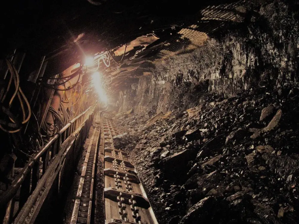 Underground coal mine tunnel with railway tracks and bright work lights illuminating the rocky walls