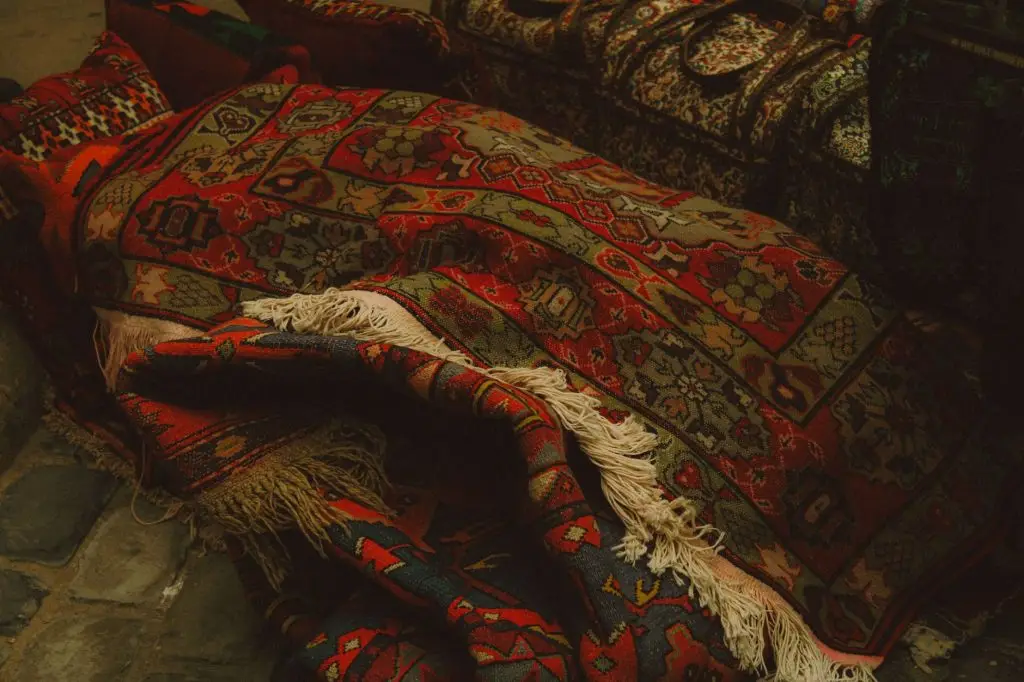 Colorful traditional rugs with ornate patterns stacked and draped with cream-colored fringe